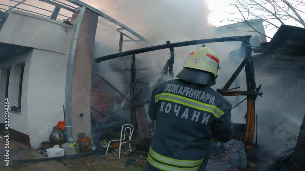 Fireman extinguishes a fire in burning house spraying water from hose Fireman extinguishes a fire in burning house spraying water from hose