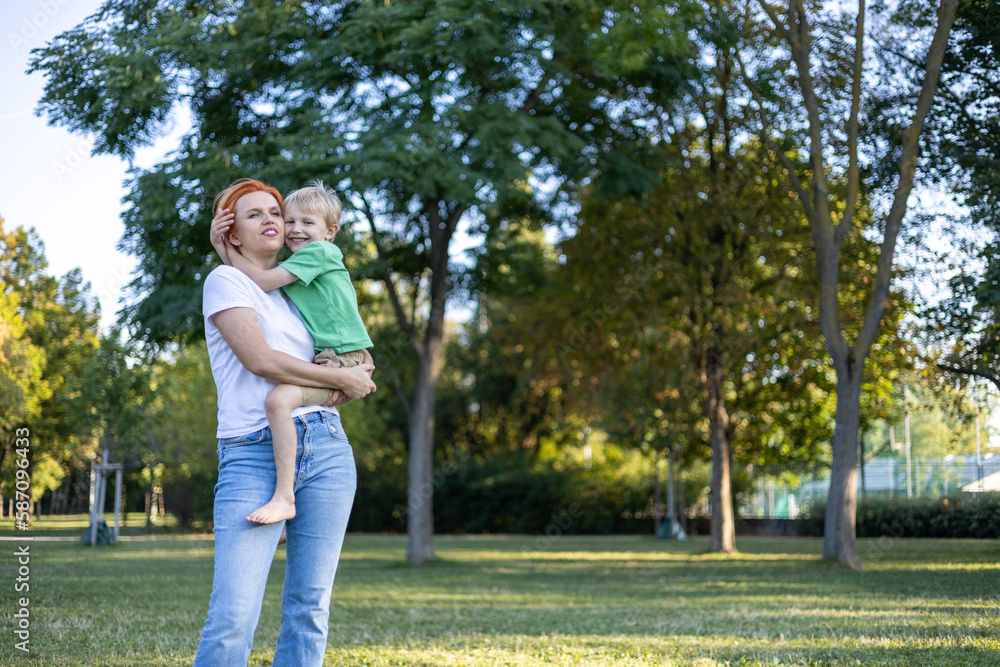 Red haired happy mother having fun with her blond haired laughing son in park