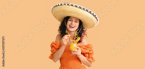 Beautiful Mexican woman in sombrero hat and with cocktail on beige background