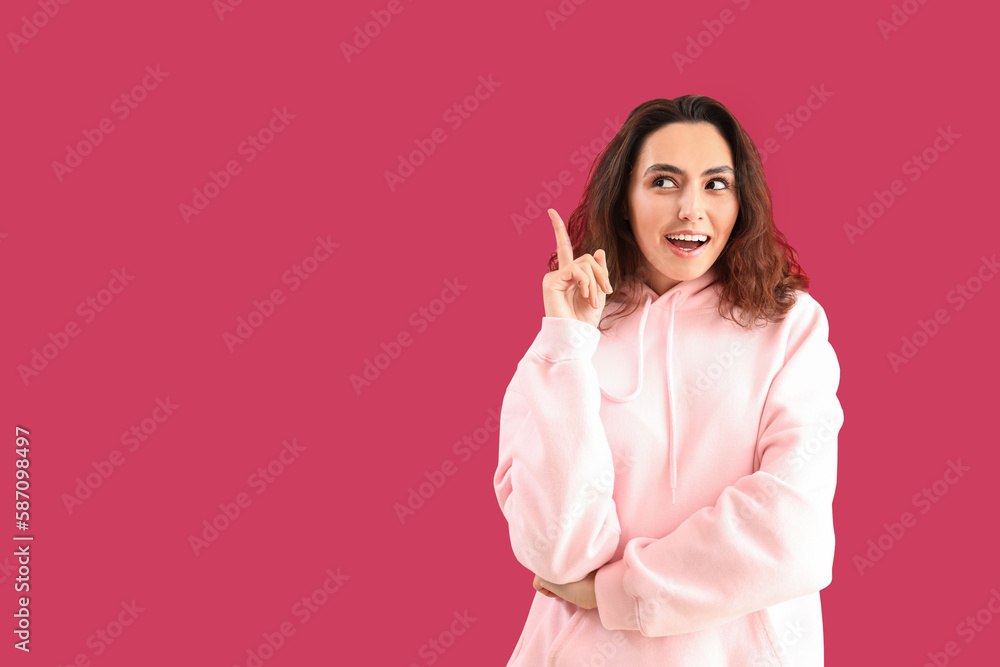 Young woman in hoodie pointing at something on pink background Young woman in hoodie pointing at something on pink background
