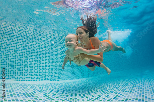 Happy family - mother, father with baby boy swimming, diving underwater with fun in blue pool. Healthy lifestyle, active parents, people water sports activity on summer vacation with child