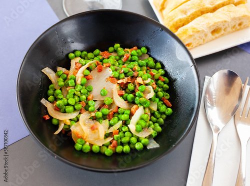 Fresh just prepared peas with ham served in bowl with onion.