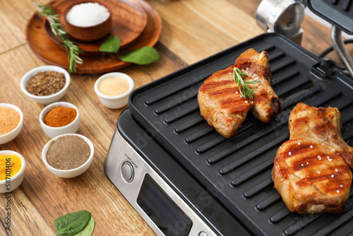 Modern electric grill with tasty steaks and spices on table