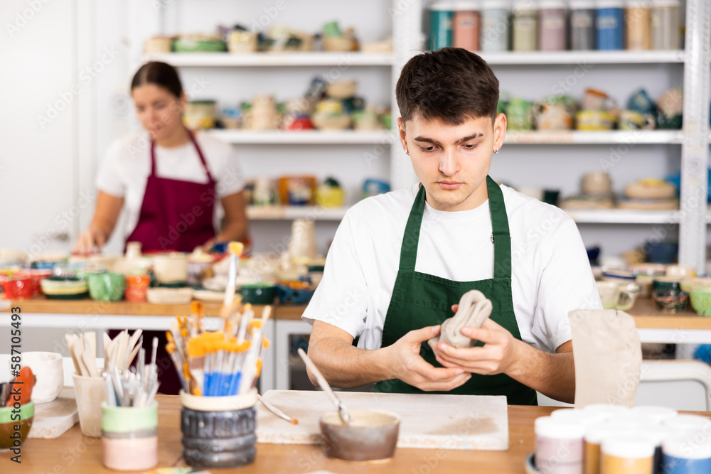Fototapeta premium Young man in apron modeling clay pottery in workshop
