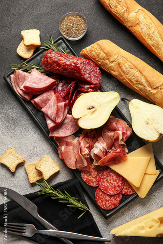 Board with assortment of tasty deli meats, cheese and bread on grunge background