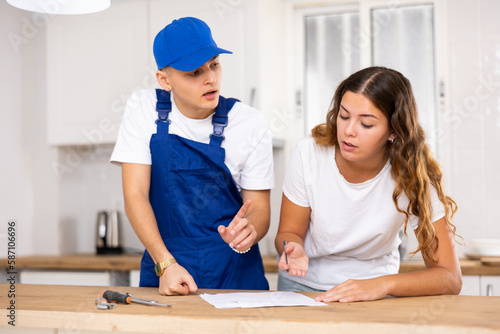 Positive professional plumber tells an young housewife where to sign an invoice for work performed.