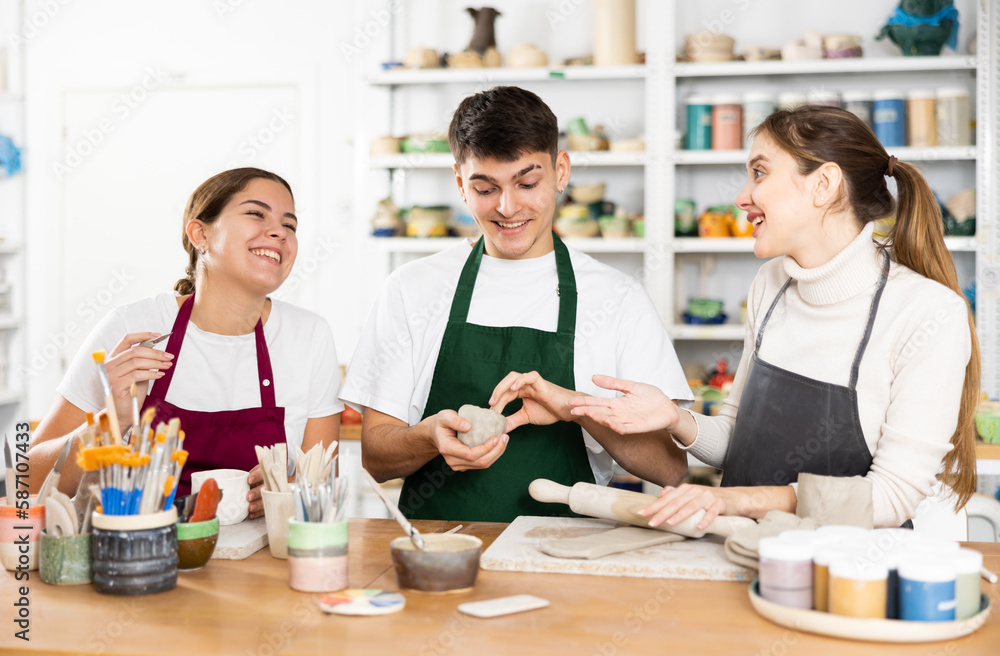 Fototapeta premium Two young women and young man making clay pottery in workshop