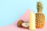Glass bottle of tasty pineapple smoothie, straw and coconut on colorful background