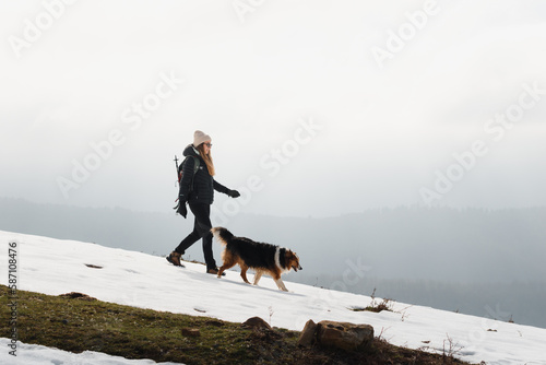 Girl with winter clothes walking with her dog in the mountains covered by snow 