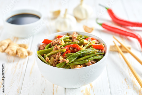 Traditional Chinese food, Szechuan style pork with green beans ginger and hot peppers on a white wooden table.