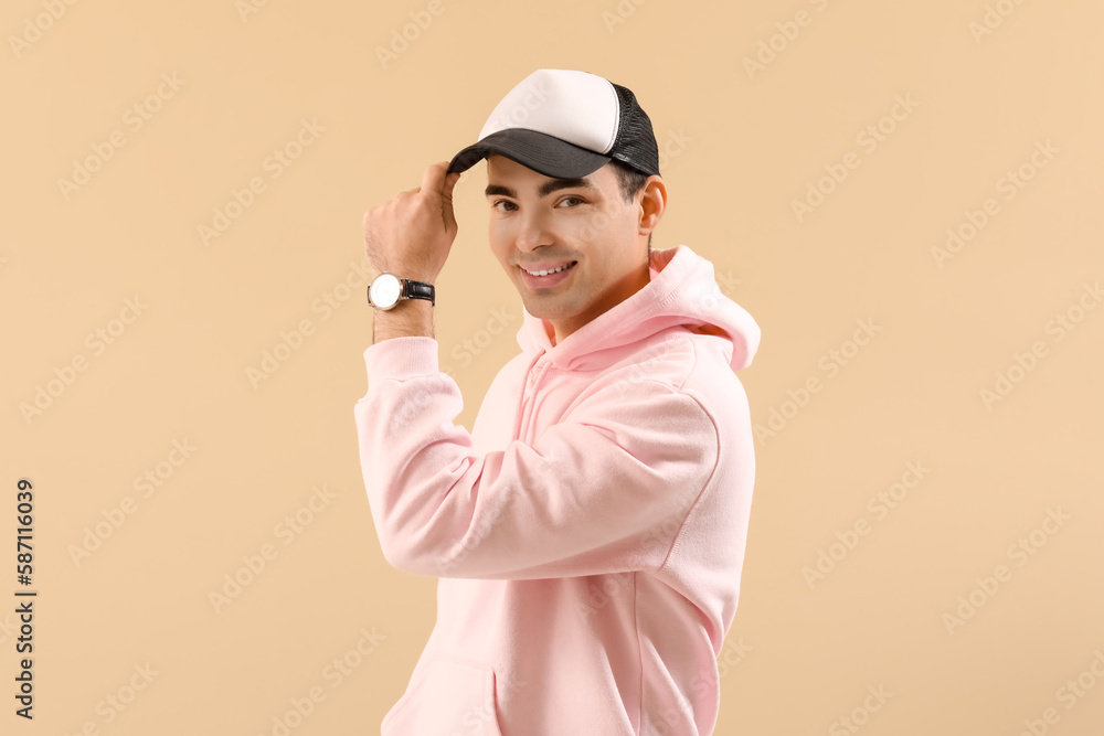 Stylish young man in hoodie and cap on beige background Stylish young man in hoodie and cap on beige background