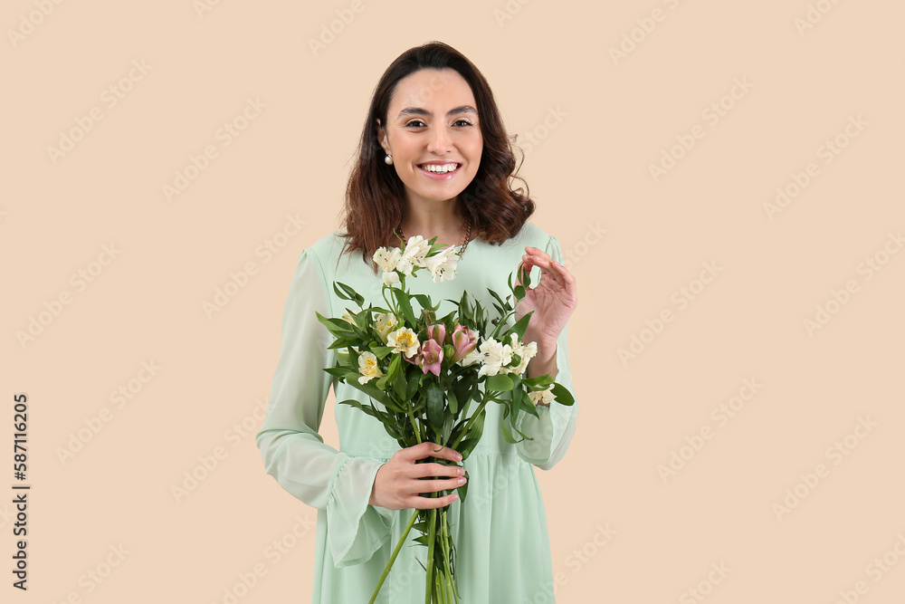 Young woman in dress with alstroemeria flowers on beige background