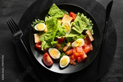Plate of delicious salad with boiled eggs and salmon on black grunge background