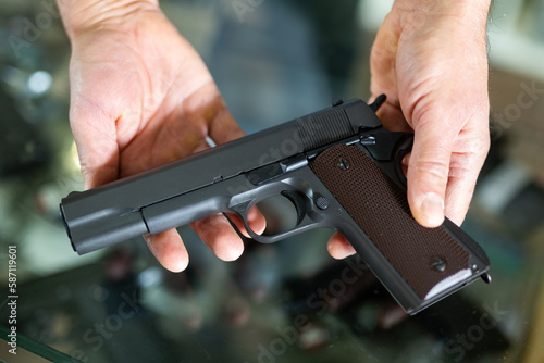 Gunsmith shop assistant demonstrates black pistol in his hands