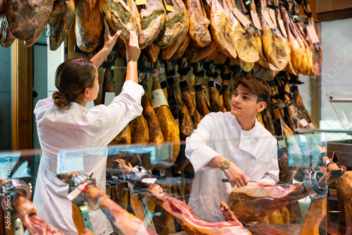 Young couple work together in butcher shop - they cut the traditional Spanish jamon