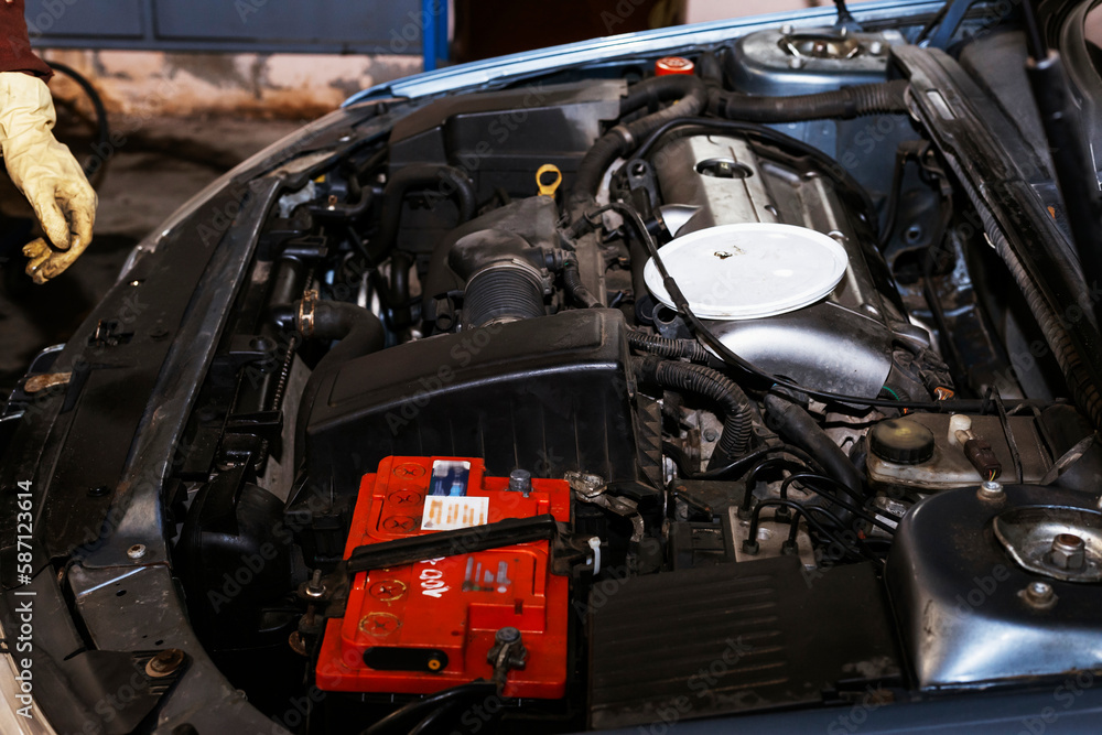 A hand of a mechanic with oil stains. The mechanic is working under the hood of a car in the workshop. Close-up of the engine with the hood open.