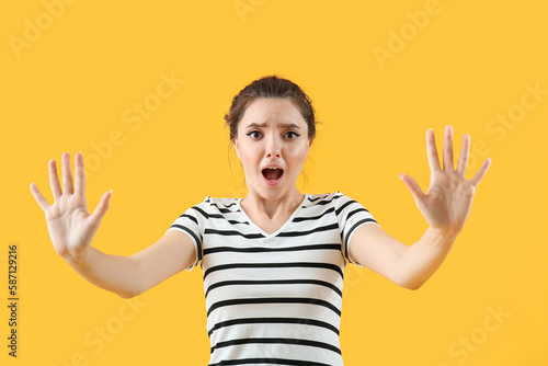 Scared young woman on yellow background