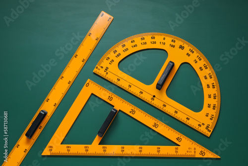 Protractor, triangle and ruler on green chalkboard, flat lay