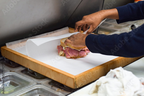 Fotografie Hands of female diner employee wrapping deli meat sandwich for takeout order