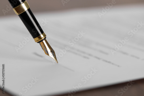 Writing on document with fountain pen at wooden table, closeup and space for text. Notary contract