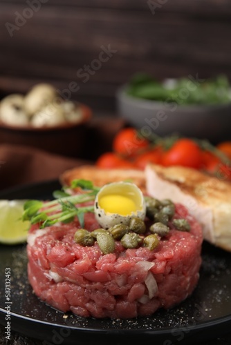 Tasty beef steak tartare served with quail egg and other accompaniments on black plate, closeup