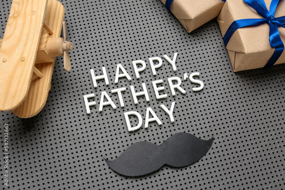 Obraz premium Text HAPPY FATHER'S DAY, wooden plane, paper mustache and gifts on board, closeup