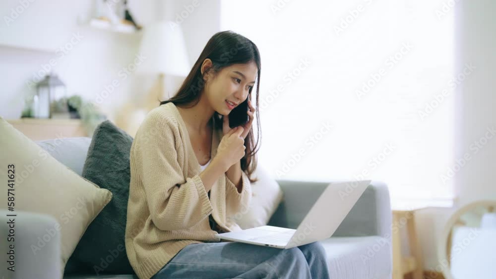 Young asian woman using computer laptop and mobile smartphone while seated on couch at home Young asian woman using computer laptop and mobile smartphone while seated on couch at home