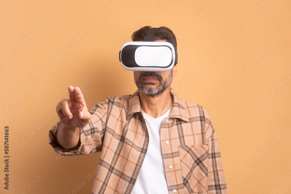 happy mature man Using VR headset and gesturing in beige background. virtual reality, technology simulation concept. happy mature man Using VR headset and gesturing in beige background. virtual reality, technology simulation concept.