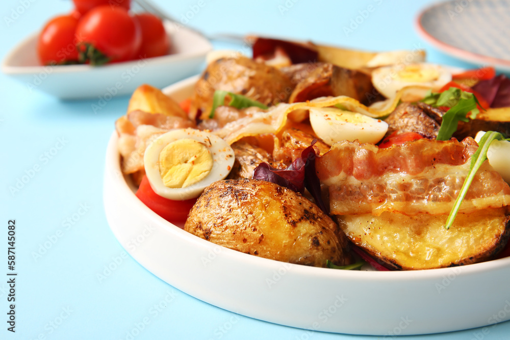 Plate of tasty potato salad with eggs, tomatoes and bacon on light blue background, closeup