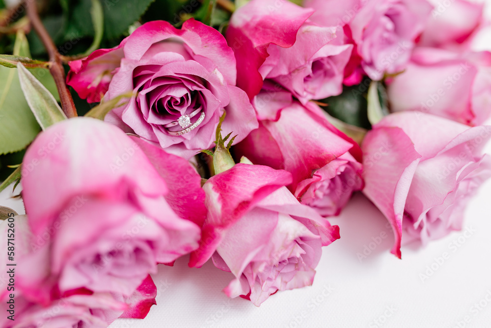 A bouquet of beautiful pink roses with a white gold engagement ring with diamonds on a white background. Fresh flowers on a white canvas. Wedding bouquet and wedding rings. Surprise marriage proposal. A bouquet of beautiful pink roses with a white gold engagement ring with diamonds on a white background. Fresh flowers on a white canvas. Wedding bouquet and wedding rings. Surprise marriage proposal.