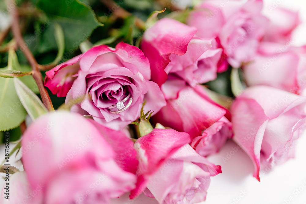 Obraz premium A bouquet of beautiful pink roses with a white gold engagement ring with diamonds on a white background. Fresh flowers on a white canvas. Wedding bouquet and wedding rings. Surprise marriage proposal.
