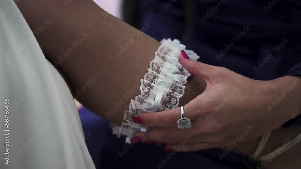 Woman placing a white garter on a bride's leg. Cinematic shot in slow motion. Woman placing a white garter on a bride's leg. Cinematic shot in slow motion.