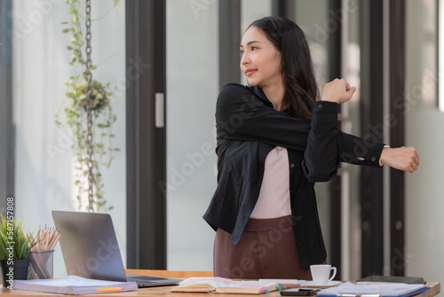 An Asian businesswoman feels tired from hard work, thus doing arm-stretching postures to relax their body. Tired Asia woman stretching her hands while working in an office.