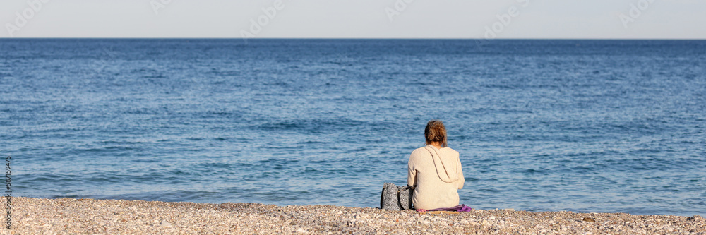 Lonely woman sits with back and looks at sea