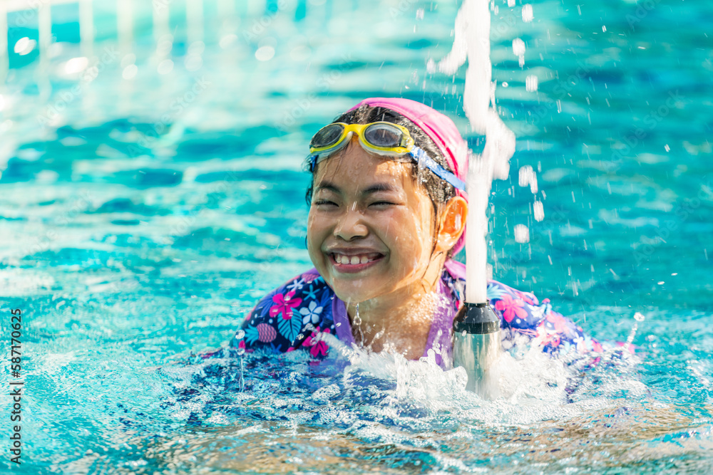 Asian cute child girl in the swimming pool, playing a small fountain in ...