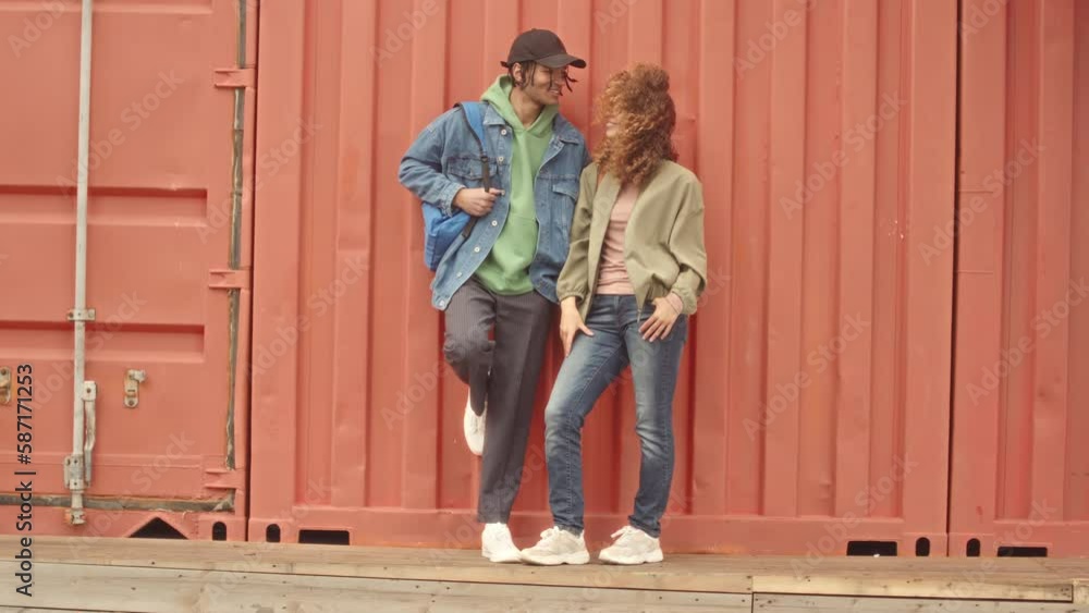 Full length slowmo portrait of cool multiracial university couple in stylish casualwear posing for camera outdoors Full length slowmo portrait of cool multiracial university couple in stylish casualwear posing for camera outdoors