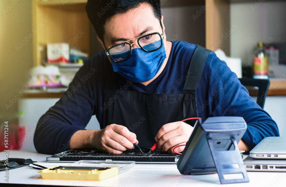 Computer technician wearing goggles and mask A laptop motherboard repairman is using an IC meter to find defects on the motherboard for repair on his workbench. Board repair with modern technology Computer technician wearing goggles and mask A laptop motherboard repairman is using an IC meter to find defects on the motherboard for repair on his workbench. Board repair with modern technology