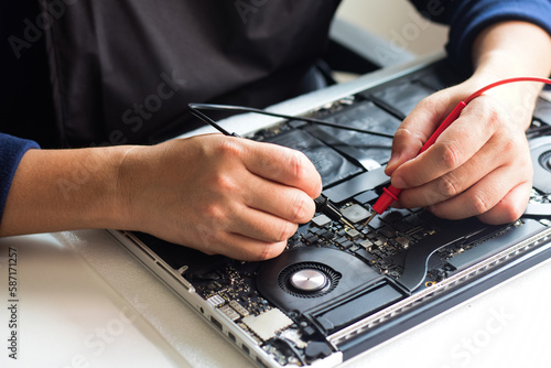 Computer technician wearing a mask A laptop motherboard repairman is using an IC meter to find defects on the motherboard for repair on his workbench. Board repair with modern technology photo