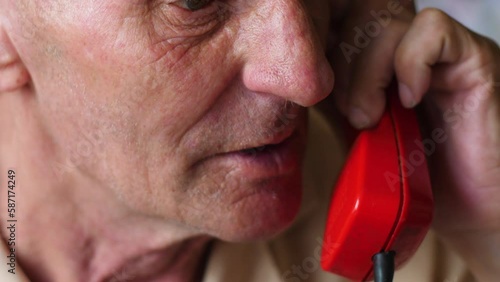portrait of caucasian old man 70 -79 years old talking on vintage red telephone.real people,old people concept.nursing home. old age photo
