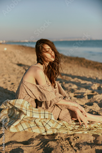 a woman near the sea sits on a blanket and looks into the distance in windy weather