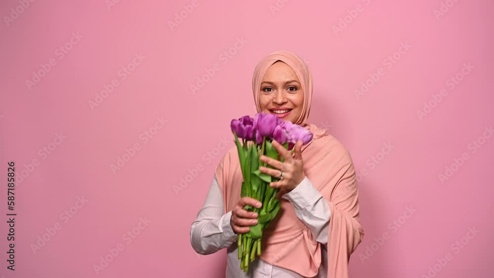 Beautiful Arab Muslim woman in pink hijab, holding bouquet of purple tulips for special festive occasion, smiling looking at camera, isolated on pink background. International Women's and Mother's Day Beautiful Arab Muslim woman in pink hijab, holding bouquet of purple tulips for special festive occasion, smiling looking at camera, isolated on pink background. International Women's and Mother's Day