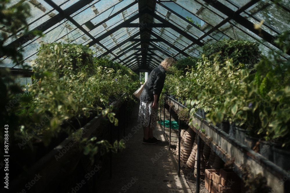 A woman bent over and sniffing the plants in the greenhouse