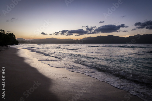 Carribean beach and waves at sunset with mountains in distance