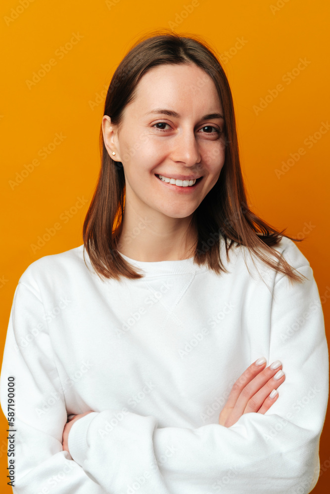 Vertical portrait of a young woman with arms crossed smiling at the camera over yellow background. Vertical portrait of a young woman with arms crossed smiling at the camera over yellow background.