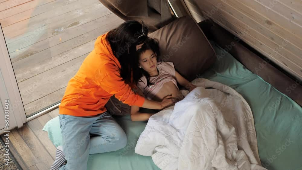 A woman palpates the spasming stomach of her daughter lying on the bed by the window, A woman palpates the spasming stomach of her daughter lying on the bed by the window,