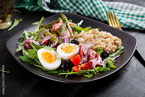 Breakfast oatmeal porridge with boiled egg, cherry tomatoes, asparagus and arugula. Healthy balanced food.