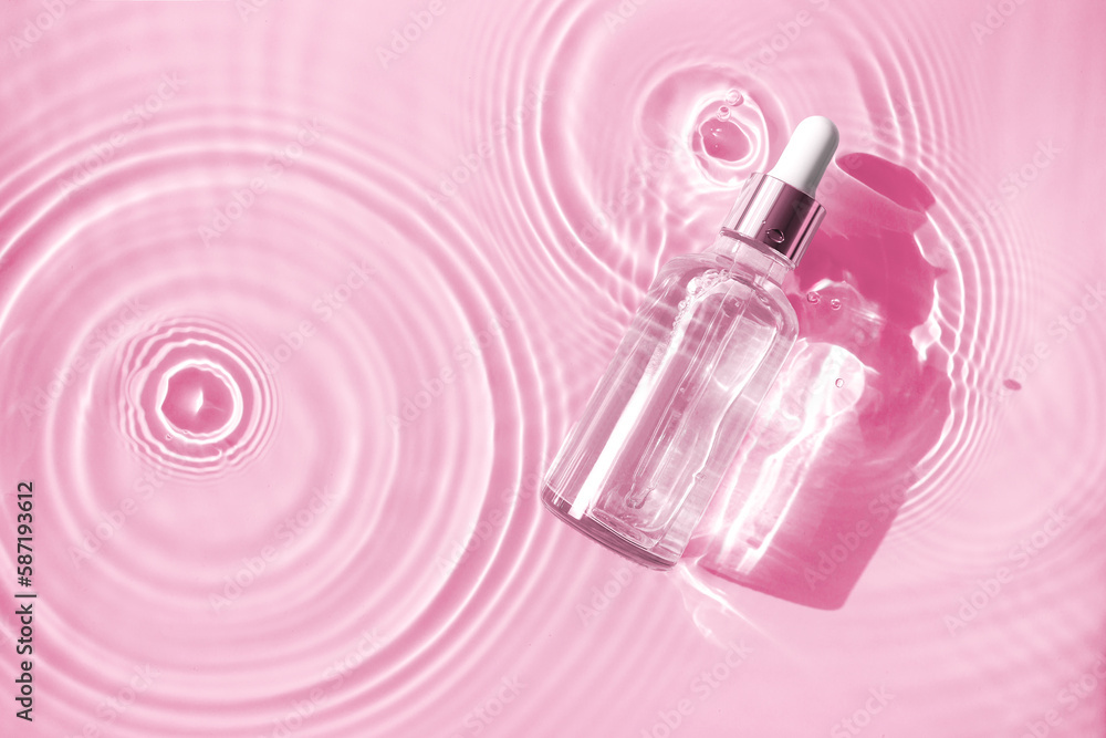 bottle of serum in water with splashes and waves on a pink background bottle of serum in water with splashes and waves on a pink background