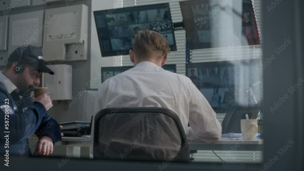 Security officer drinks coffee with coworker monitoring CCTV cameras. Security guard uses walkie talkie and landline phone. View from surveillance cameras displayed on computer screens in program. Security officer drinks coffee with coworker monitoring CCTV cameras. Security guard uses walkie talkie and landline phone. View from surveillance cameras displayed on computer screens in program.