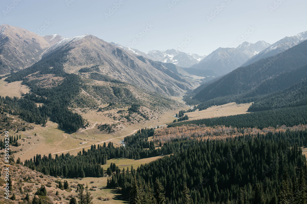 The photo depicts a mountain gorge covered with forest and green grass, with a road visible in the distance. The photo depicts a mountain gorge covered with forest and green grass, with a road visible in the distance.