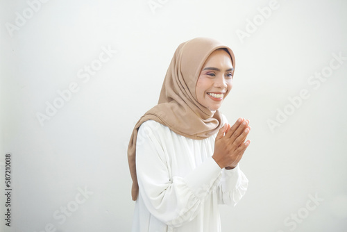 Young Asian Islam woman wearing headscarf gives greeting hands at with a big smile on her face. Indonesian woman on gray background. Eid Mubarak, Eid Fitr, Ramadan